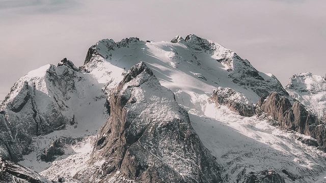 Snow-covered mountain range under cloudy sky Snowy mountain peaks with cloudy sky